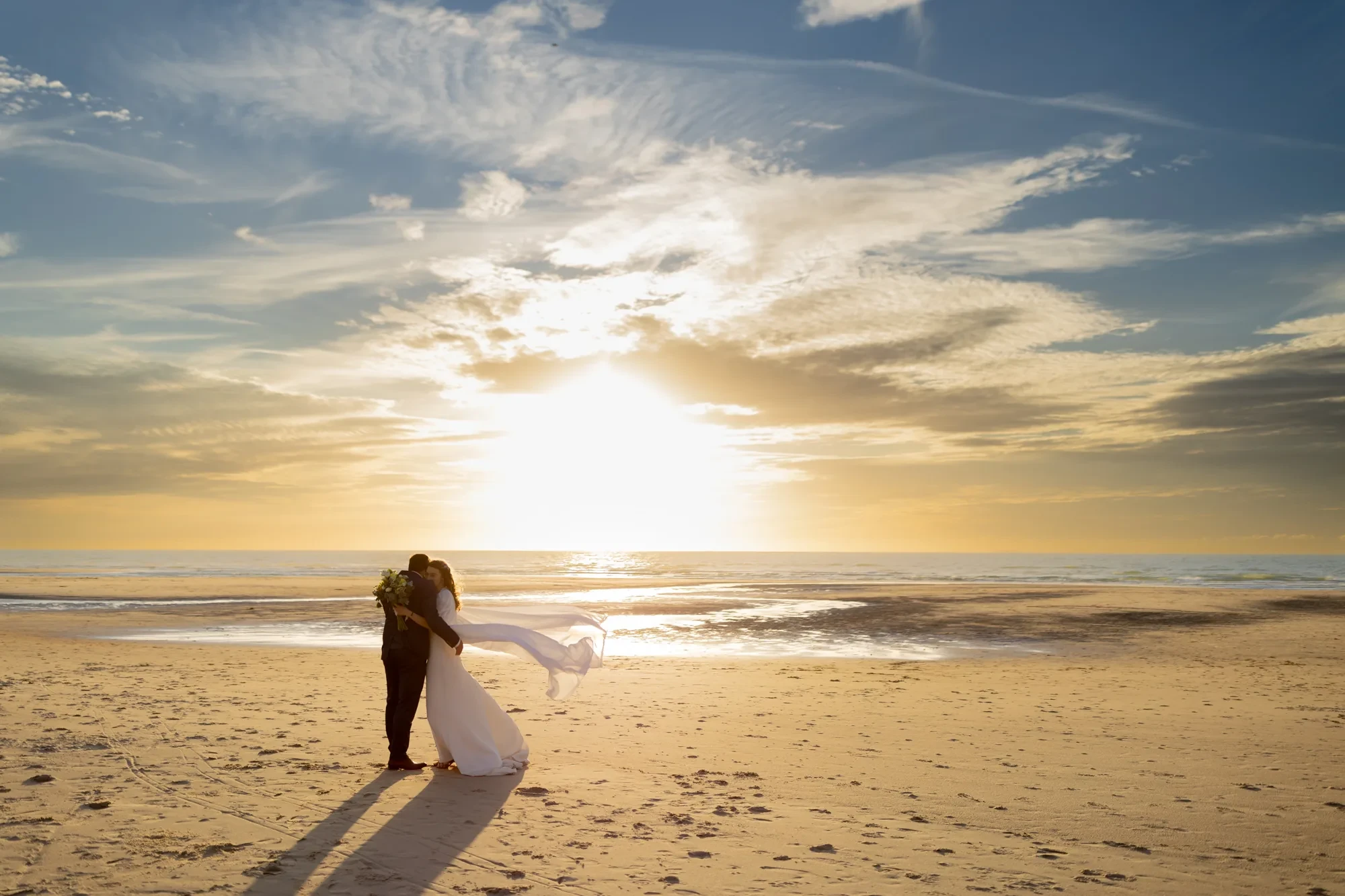 newlyweds-embrace-beach-sunset.webp