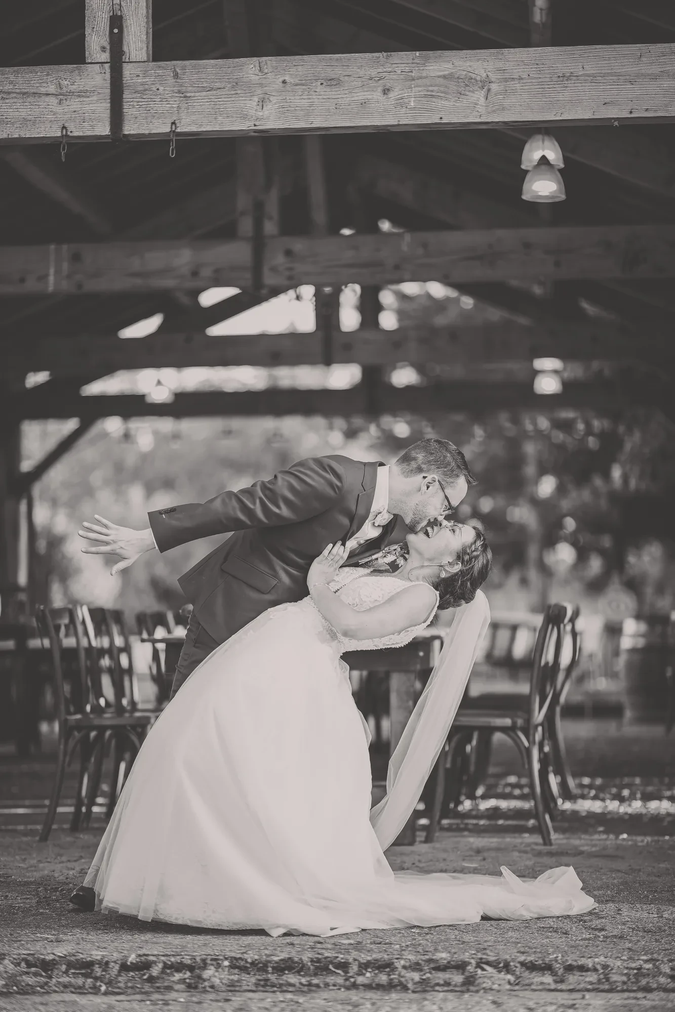 newlyweds-dip-kiss-barn-bw.webp